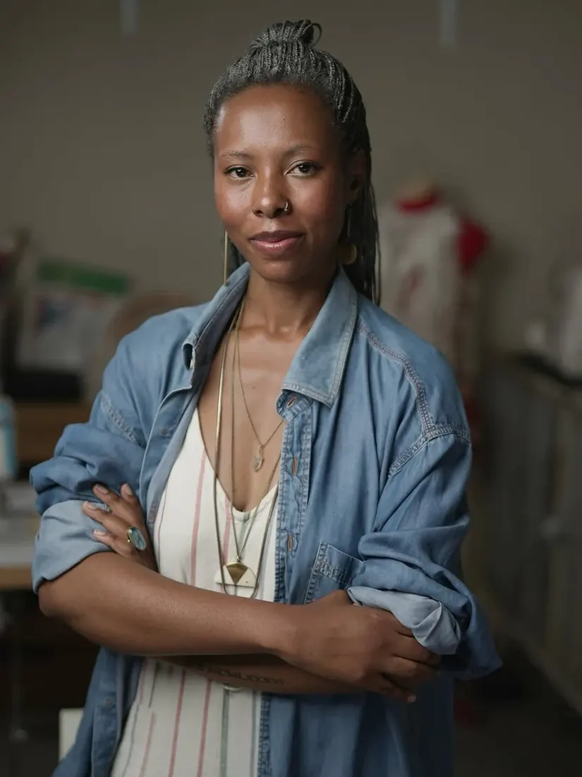 Portrait of Danayi Chapfika-Madondo, arms folded, in a denim shirt in the studio
