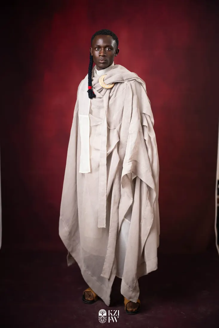 Model in pale layered garment with sculpted fabric ruffles, standing against granite