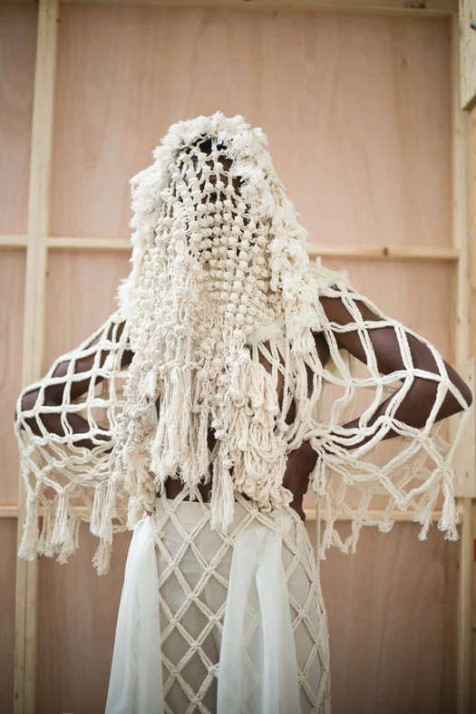 Macramé and knotted cotton garment with tassels, worn over white cloth