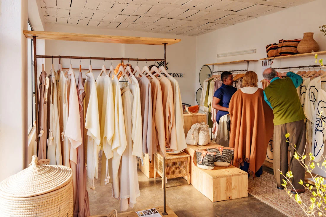 Inside the Haus of Stone Showroom — cream garments on wooden rails, woven baskets and pine plinths